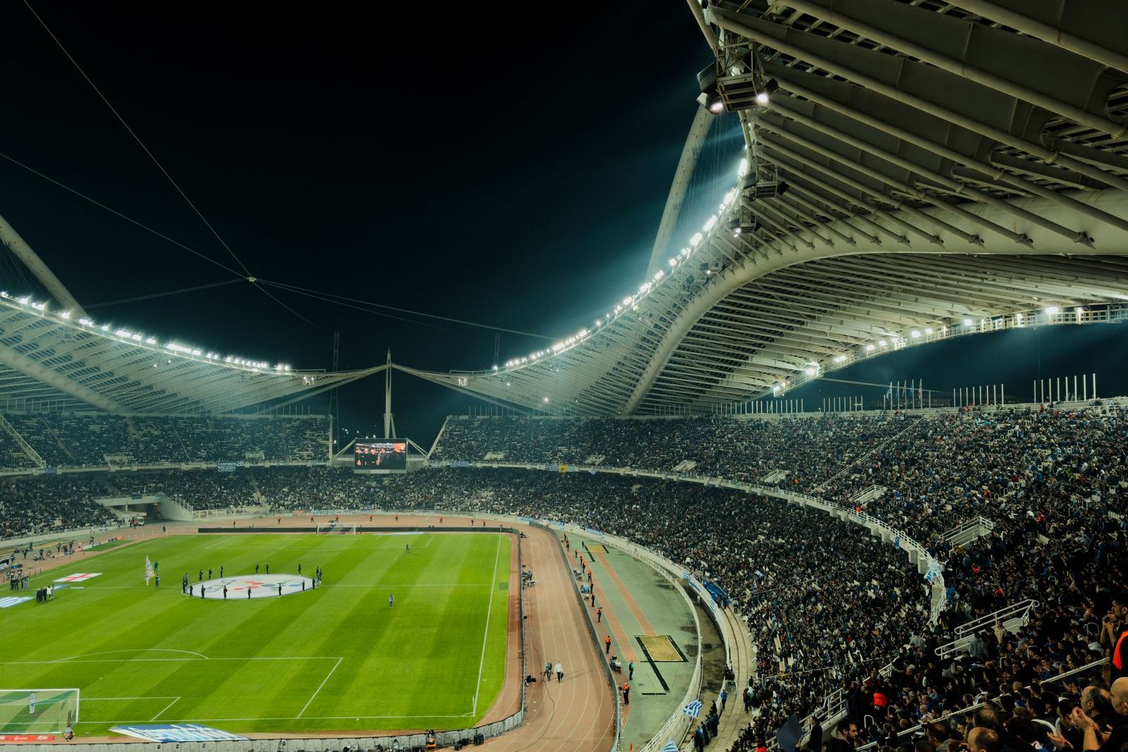 A floodlit football stadium at night with crowded stands